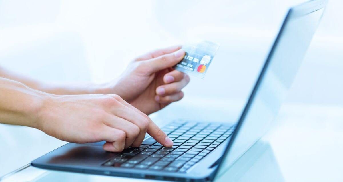 Image of a person holding a credit card and typing on a laptop to execute an online upfront payment